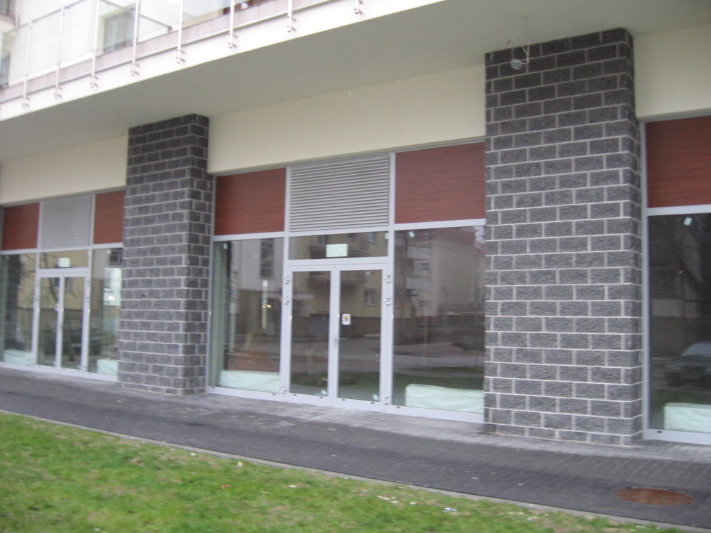 Elewacja lokalu użytkowego z dużymi witrynami i kolumnami z szarej cegły, widok z poziomu trawnika.